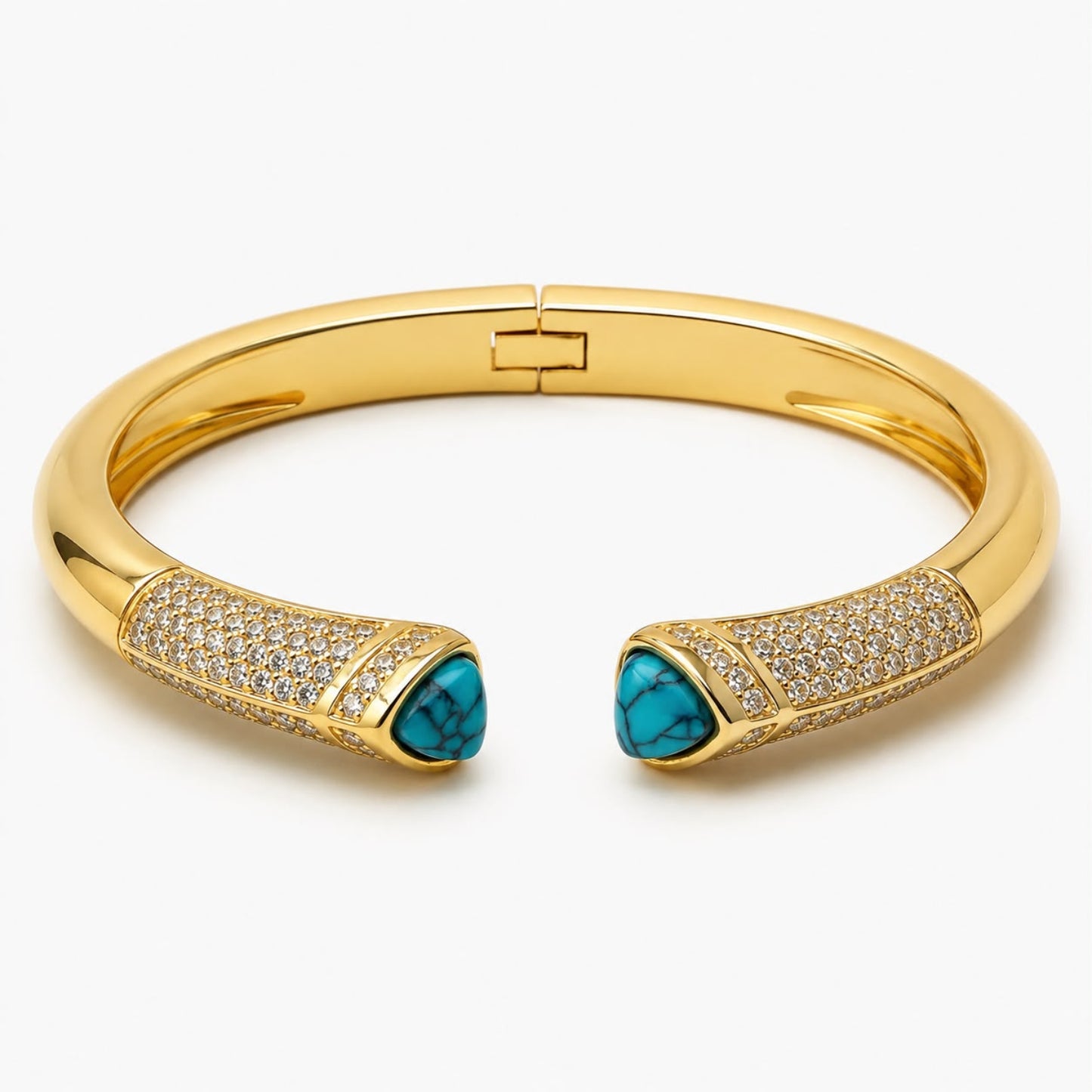 A gold cuff bracelet with pavé-set clear stones and two turquoise-colored triangular accents at the ends, shown on a light gray background.